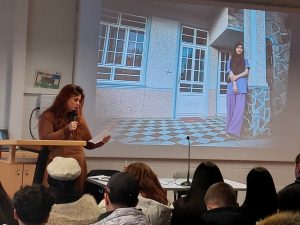 Auf dem Bild ist im Vordergrund Alea Horst zu sehen. Im Hintergrund kann man ein Mädchen allein in einem Innenhof erkennen.